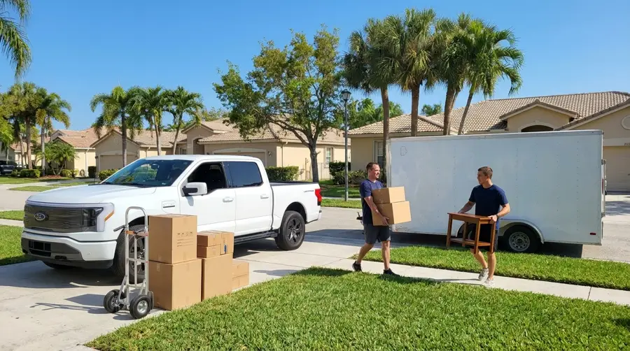 Two movers walking furniture down a Florida sidewalk to the truck